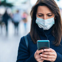 Portrait of young woman on the street wearing  face protective mask to prevent Coronavirus and anti-smog and using smartphone